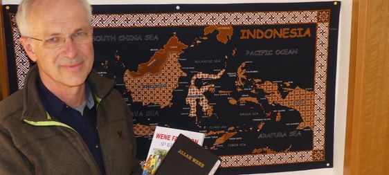 Pfarrer Friedrich Tometten mit der kompletten Bibel in die Yali-Sprache und der Kinderbibel vor einer Karte, die auf der rechten Seite West-Papua als Teil der Republik Indonesien zeigt. (Foto: Ingrid Weiland)