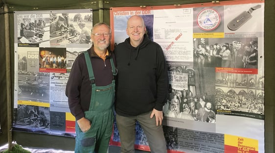 Der Lüdenscheider Diplom-Designer Bernd Drescher (r.) und der frühere stellvertretende Generalsekretär des CVJM-Gesamtverbandes in Deutschland, Albrecht Kaul (l.) , der über 40 Jahre in der DDR gelebt hat, haben das „Zelt der Begegnung“ aus einem Original-Zelt der NVA erstellt. Im Hintergrund sind Bilder aus der Ausstellung „31 Jahre friedliche Revolution – Ein Zelt erzählt vom Wunder Gottes 1989“ zu sehen. (Foto: Ingrid Weiland)