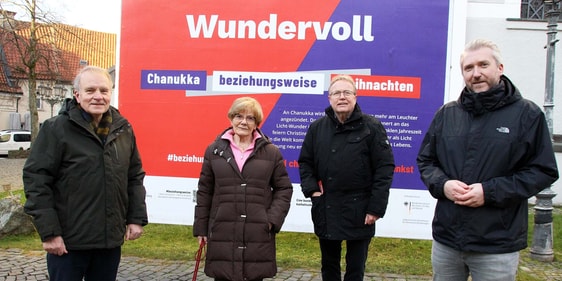 Vor dem Großplakat "Wundervoll: Chanukka beziehungsweise Weihnachten" sprachen Matthias Wagner, Hella Goldbach, Achim Riggert und Bürgermeister Sebastian Wagemeyer (v.l.) über jüdisches Leben in Deutschland und in der Region. (Foto: Jakob Salzmann)